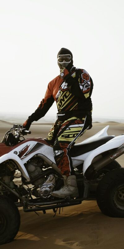 A male rider on an ATV navigating the sand dunes during the day, wearing protective gear and a helmet.