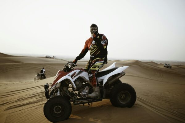 A male rider on an ATV navigating the sand dunes during the day, wearing protective gear and a helmet.