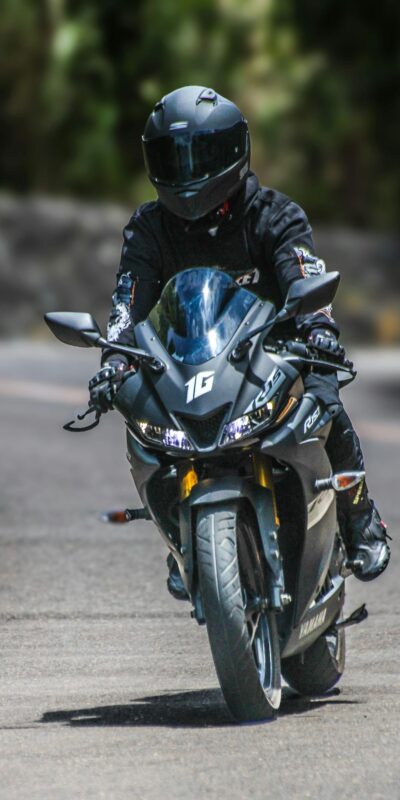 A motorcyclist in gear rides a Yamaha YZF-R15 on a curved road during daylight.