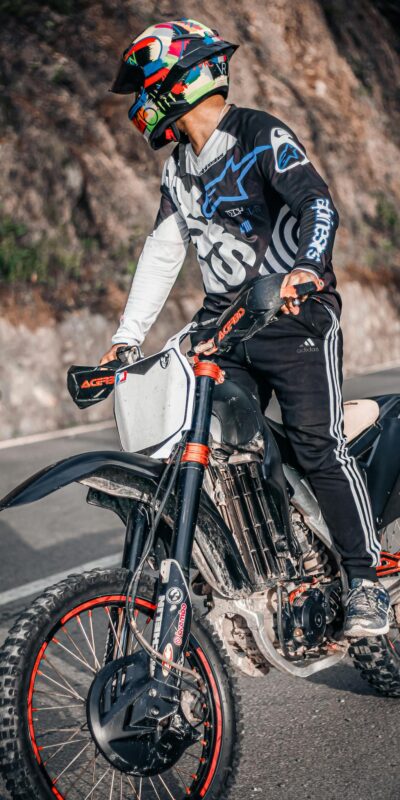 Biker in full gear rides a motorcycle on a curved mountain road, dressed for high-speed adventure.