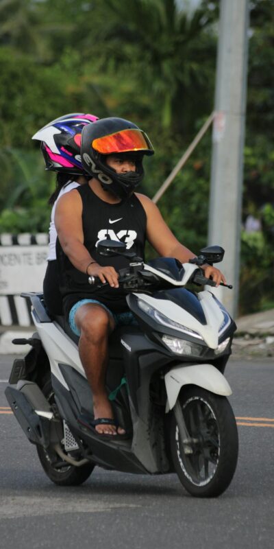 Motorcyclist and passenger wearing helmets riding on a city street.