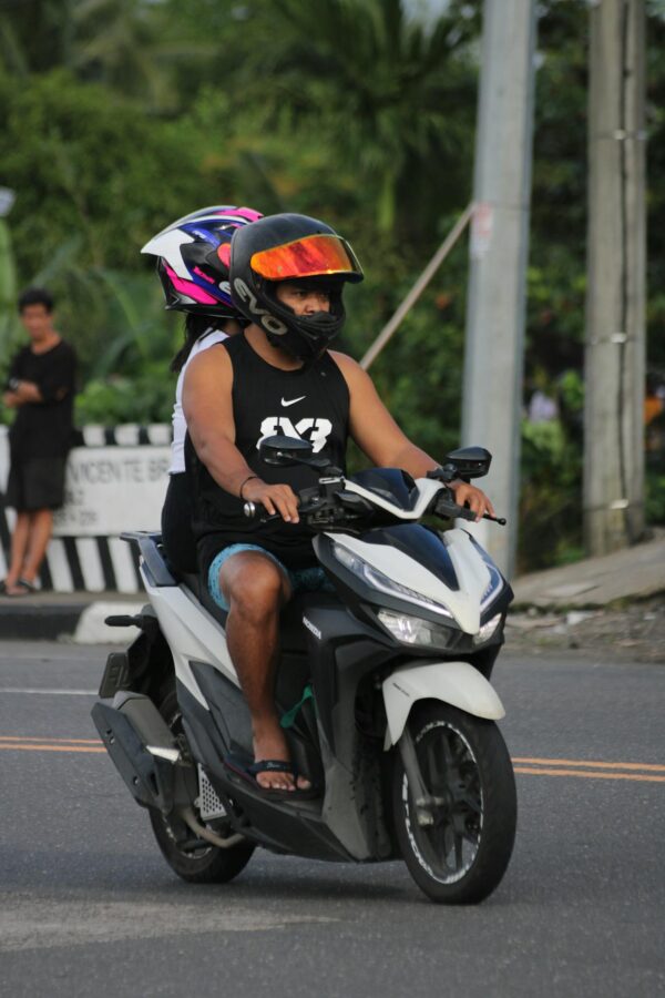 Motorcyclist and passenger wearing helmets riding on a city street.